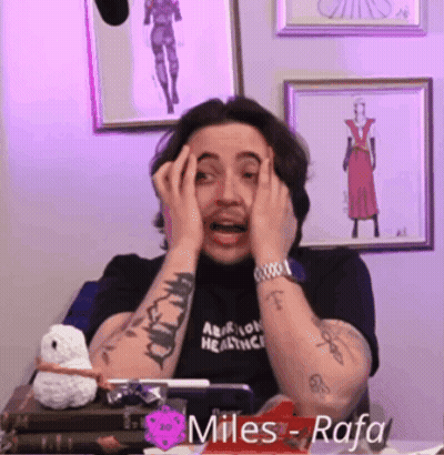 A Man With A Tattoo On His Arm Is Covering His Face With His Hands While Wearing A Black Shirt That Says Miles Rafa GIF