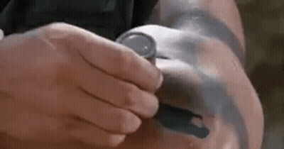 A Man With A Tattoo On His Arm Is Holding A Watch . GIF