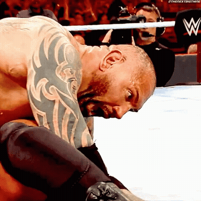 A Man With A Tattoo On His Arm Is Kneeling Down In A Wrestling Ring With A W Logo In The Background GIF