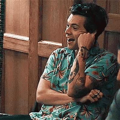 A Man With A Tattoo On His Arm Is Sitting In A Chair With His Arms Crossed And Laughing . GIF
