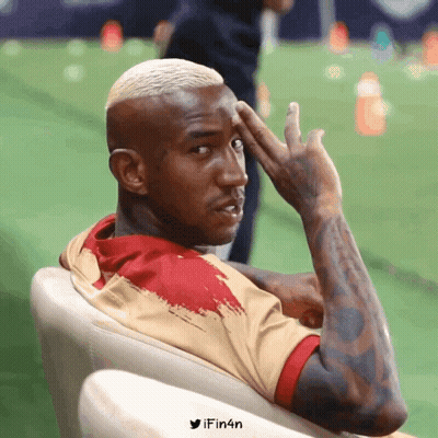 A Man With A Tattoo On His Arm Is Sitting In A Chair With His Hand On His Forehead And The Words Ifin4n Below Him GIF