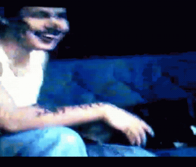 A Man With A Tattoo On His Arm Is Sitting On A Blue Couch And Smiling GIF
