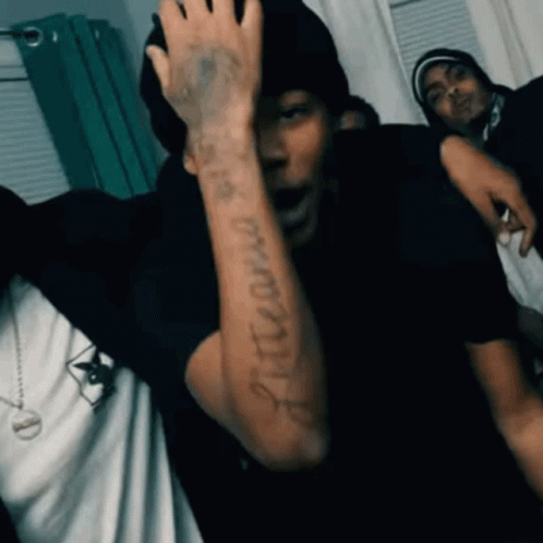 A Man With A Tattoo On His Arm Is Standing In A Room With A Group Of People . GIF