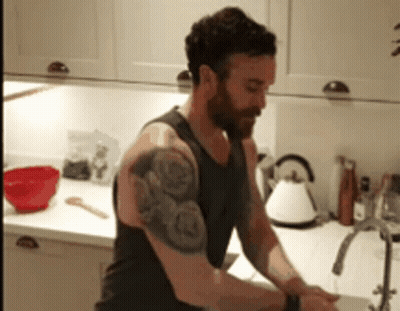 A Man With A Tattoo On His Arm Is Washing His Hands In A Kitchen GIF