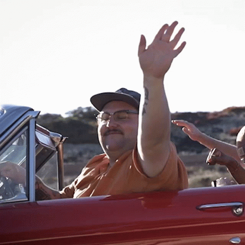 A Man With A Tattoo On His Arm Is Waving From The Window Of A Red Car GIF