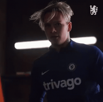 A Man With A Tattoo On His Arm Is Wearing A Blue Shirt With A Chelsea Logo On It . GIF