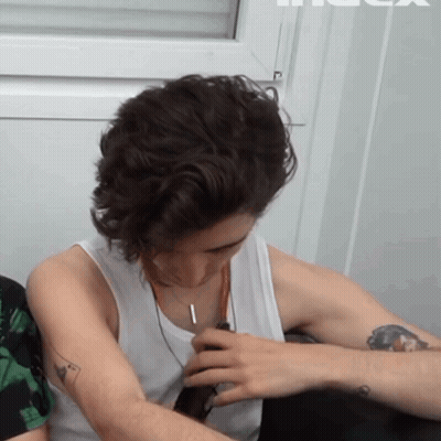 A Man With A Tattoo On His Arm Is Wearing A White Tank Top And A Necklace GIF