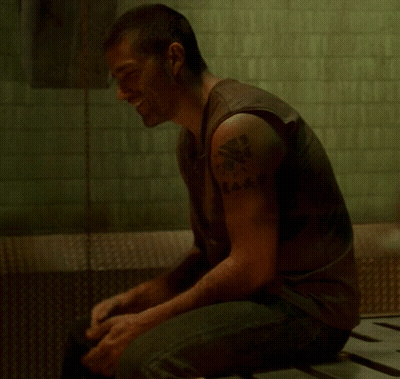 A Man With A Tattoo On His Arm Looks Down GIF