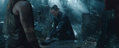A Man With A Tattoo On His Arm Sits On A Wooden Table In A Dark Forest GIF