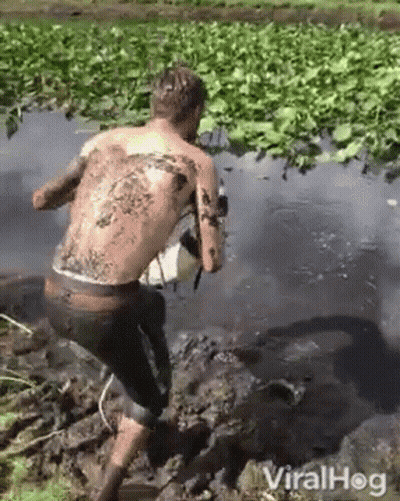 A Man With A Tattoo On His Back Is Walking Through The Mud . GIF
