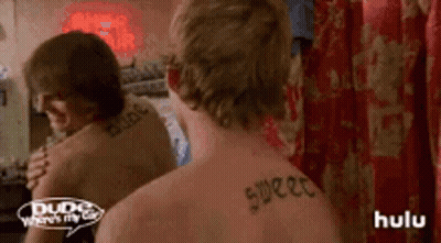 A Man With A Tattoo On His Back Looks At Himself In A Mirror . GIF