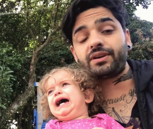 A Man With A Tattoo On His Chest Is Holding A Crying Baby GIF