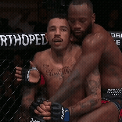 A Man With A Tattoo On His Chest Is Hugging Another Man With Ufc Gloves GIF