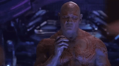 A Man With A Tattoo On His Chest Is Sitting In A Dark Room . GIF
