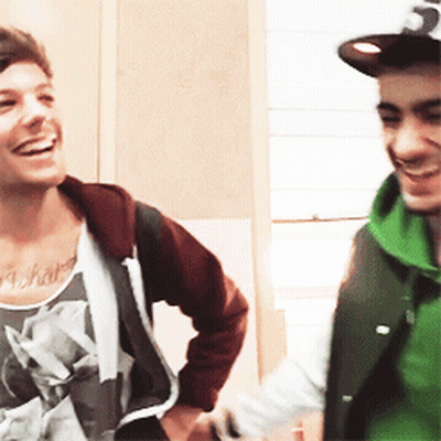A Man With A Tattoo On His Chest Is Smiling Next To Another Man Wearing A Green Vest GIF