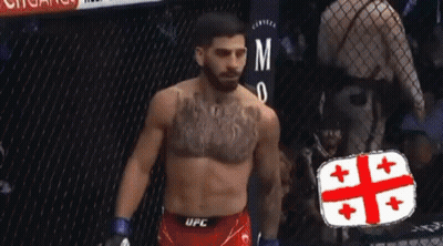 A Man With A Tattoo On His Chest Is Standing In A Cage Wearing A Pair Of Ufc Shorts . GIF