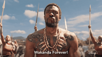A Man With A Tattoo On His Chest Stands In Front Of A Group Of People Holding Spears And Says " Wakanda Forever " GIF