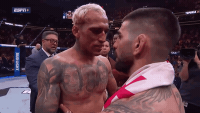 A Man With A Tattoo On His Chest Stands Next To Another Man With A Bud Light Banner Behind Him GIF