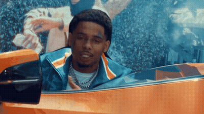 A Man With A Tattoo On His Face Is Driving An Orange Car GIF