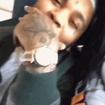 A Man With A Tattoo On His Face Is Holding A Watch In His Mouth . GIF