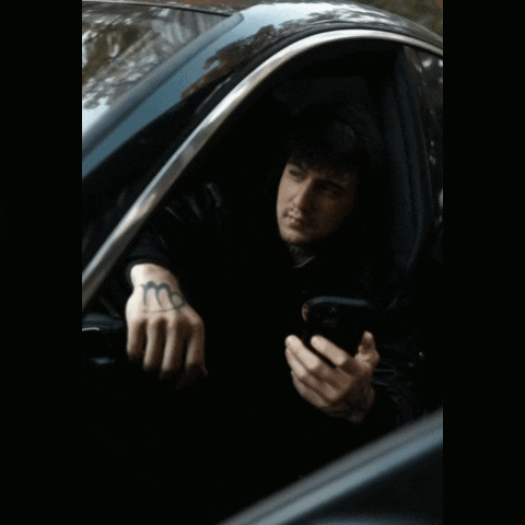 A Man With A Tattoo On His Hand Is Sitting In A Car And Looking At His Phone GIF