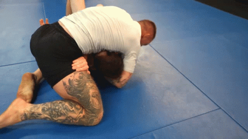 A Man With A Tattoo On His Leg Is Kneeling Down On A Blue Mat GIF