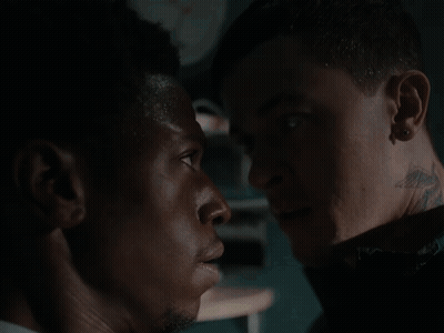 A Man With A Tattoo On His Neck Is Looking At Another Man GIF