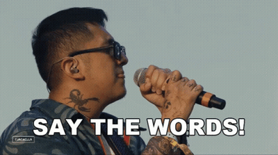 A Man With A Tattoo On His Neck Is Singing Into A Microphone With The Words Say The Words Behind Him GIF