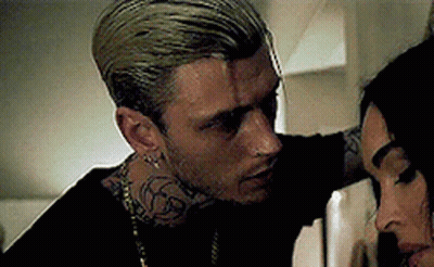 A Man With A Tattoo On His Neck Is Standing Next To A Woman . GIF