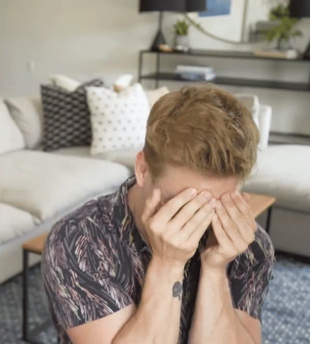 A Man With A Tattoo On His Wrist Is Covering His Face GIF
