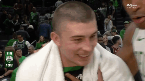 A Man With A Towel Around His Neck Is Smiling In Front Of A Scoreboard That Says 108 On It GIF
