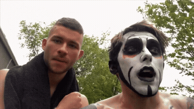 A Man With A Towel Around His Neck Is Standing Next To A Man With A Scary Face Painted On His Face GIF