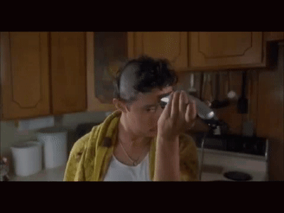 A Man With A Towel Around His Neck Is Using A Hair Straightener On His Head . GIF