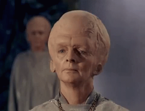 A Man With A Very Large Head Is Standing In Front Of A Group Of People . GIF