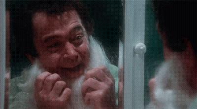 A Man With A White Beard Is Looking At Himself In A Mirror . GIF