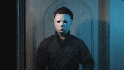 A Man With A White Mask On His Face Stands In Front Of A Door GIF