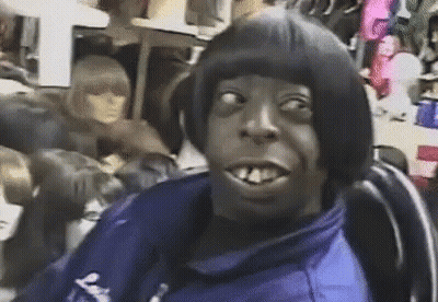 A Man With A Wig On His Head Is Sitting In A Chair In Front Of A Mannequin . GIF