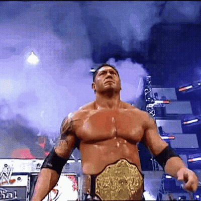 A Man With A Wrestling Belt Is Standing In Front Of A Sign That Says ' N ' On It GIF