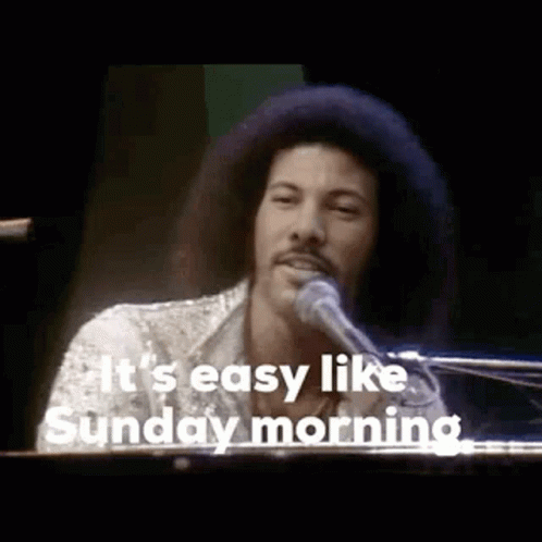 A Man With An Afro Is Singing Into A Microphone While Playing A Piano . GIF