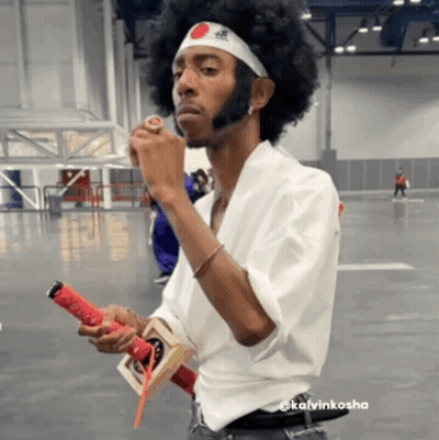 A Man With An Afro Wearing A Headband With A Red And White Circle On It GIF