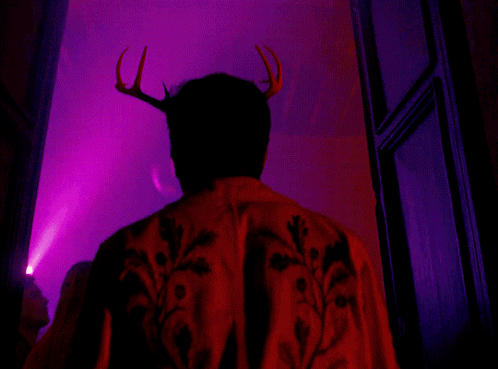 A Man With Antlers On His Head Is Standing In Front Of A Pink Light GIF