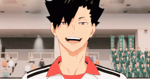 A Man With Black Hair And A Red Shirt Is Smiling In Front Of A Crowd Of People GIF
