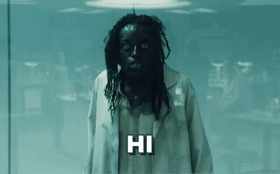 A Man With Black Hair And Dreadlocks Is Wearing A Lab Coat And A Mask And Saying Hi . GIF