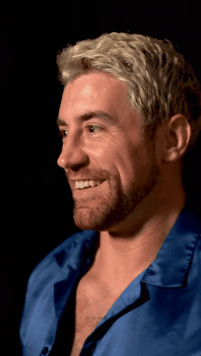 A Man With Blonde Hair And A Beard Is Smiling And Wearing A Blue Shirt GIF