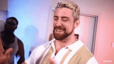 A Man With Blonde Hair And A Beard Is Smiling In Front Of A Door GIF