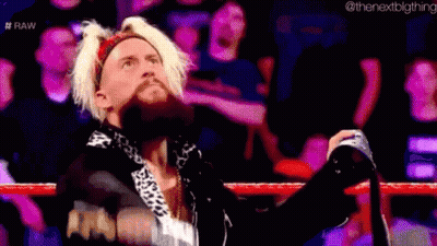 A Man With Blonde Hair And A Beard Is Standing In A Wrestling Ring With His Hands In The Air . GIF