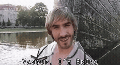 A Man With Blonde Hair And A Beard Is Standing Next To A Body Of Water And Smiling . GIF
