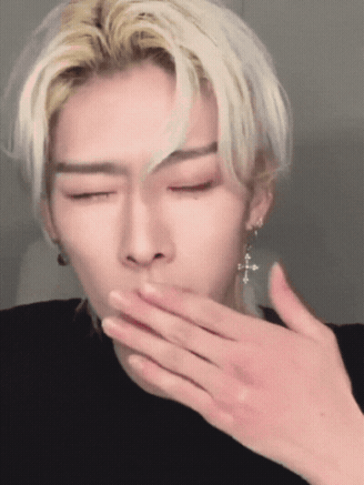 A Man With Blonde Hair And Earrings Is Covering His Mouth With His Hand GIF