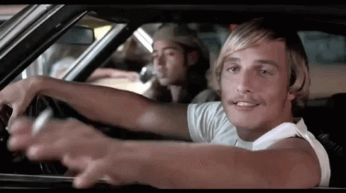A Man With Blonde Hair Is Driving A Car With Another Man In The Back Seat . GIF