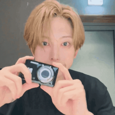 A Man With Blonde Hair Is Holding A Camera In Front Of His Face GIF